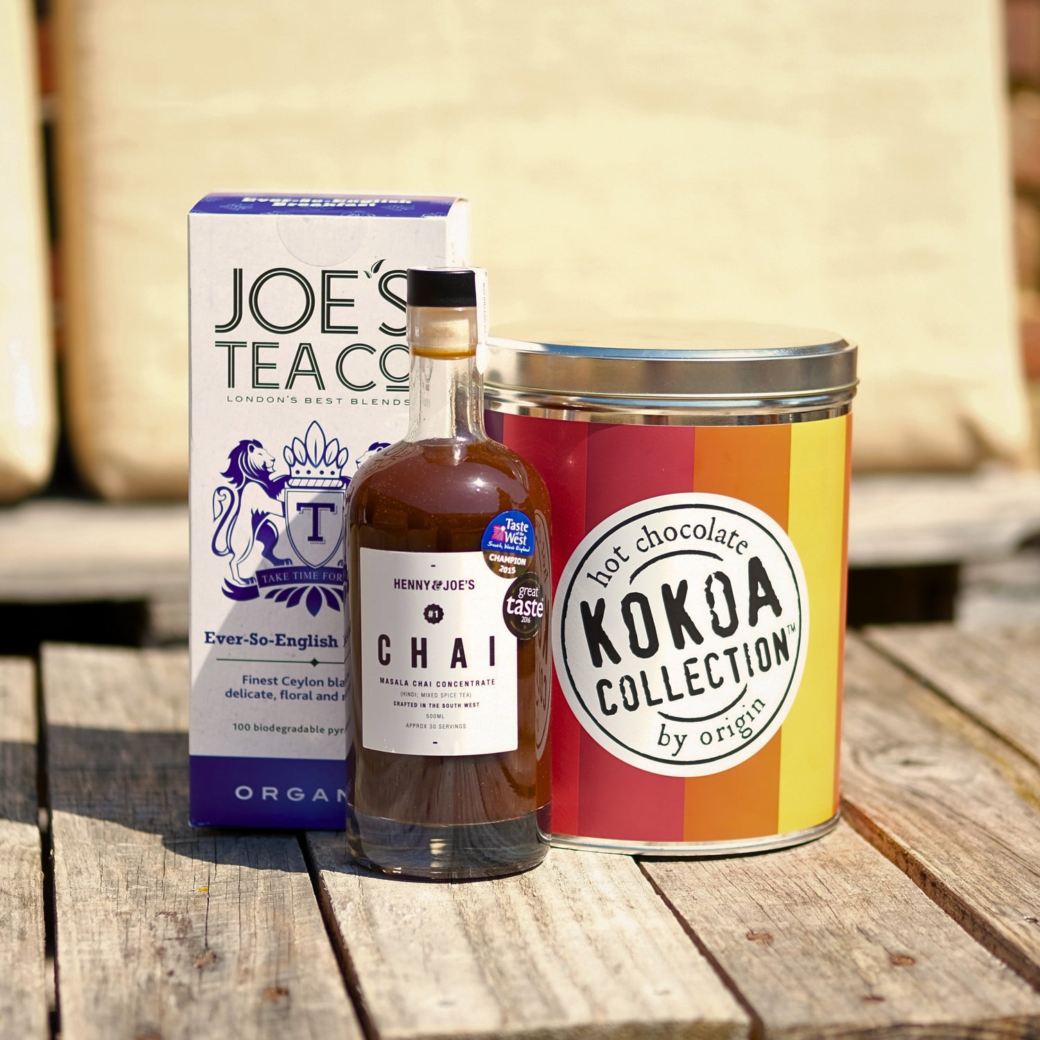 Bottle of chai, box of tea, and canister of hot chocolate on a wooden surface.